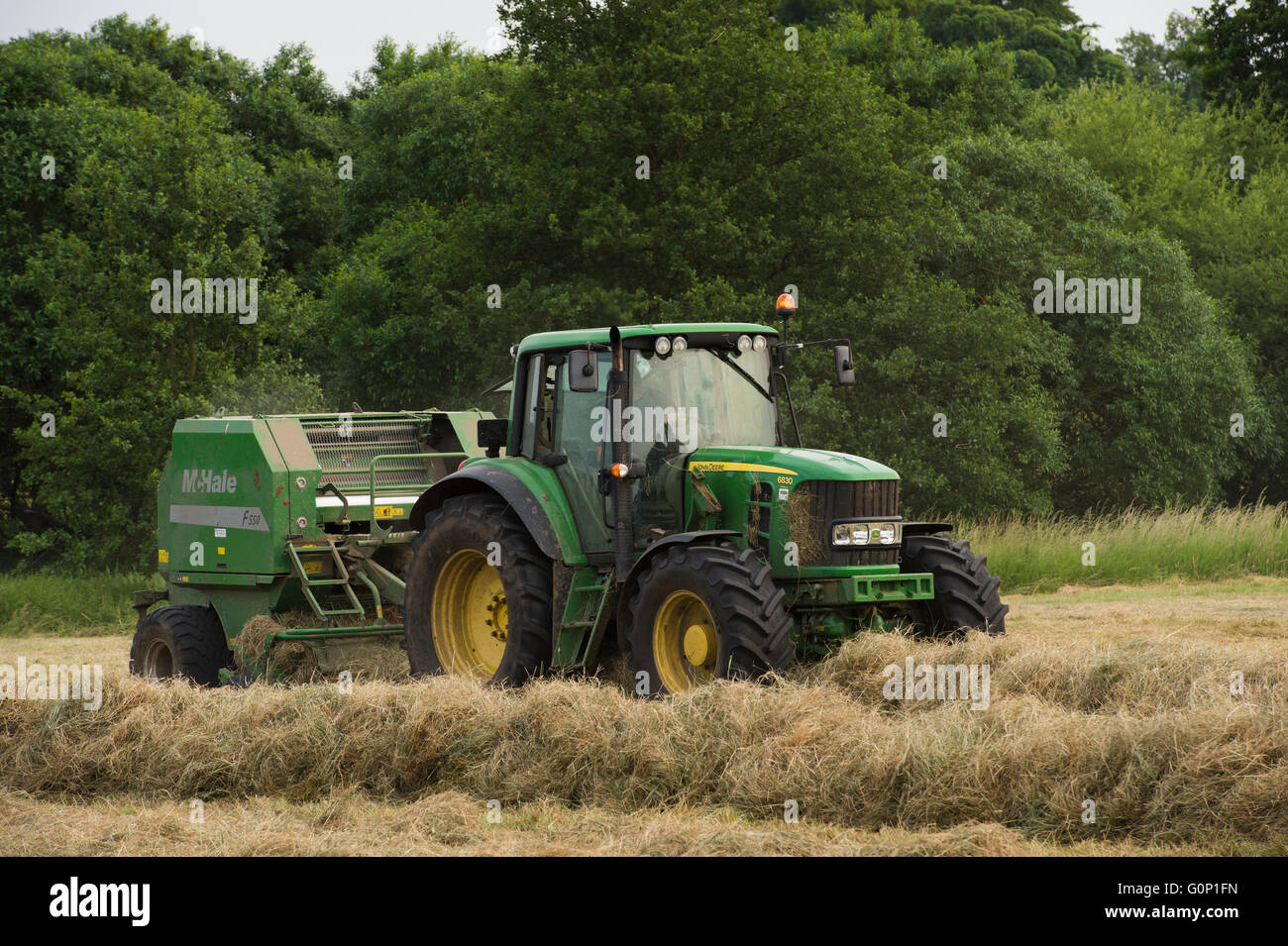 Silage making - green, farm tractor pulling a round baler, is working in a field at Great Ouseburn, North Yorkshire, England. Stock Photo