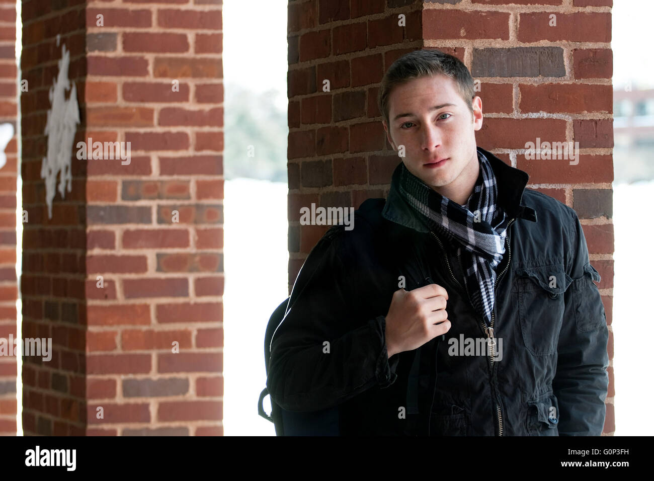 A portrait of a young man standing in an outdoor corridor with his backpack. Stock Photo