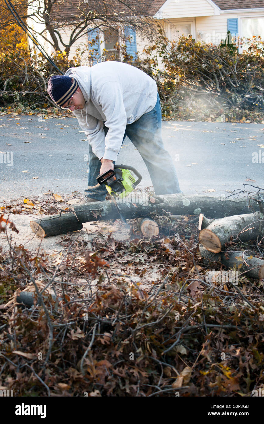 Man cutting tree limbs with a chainsaw that have fallen from storm damage.  A late fall snow storm in the month of October was t Stock Photo