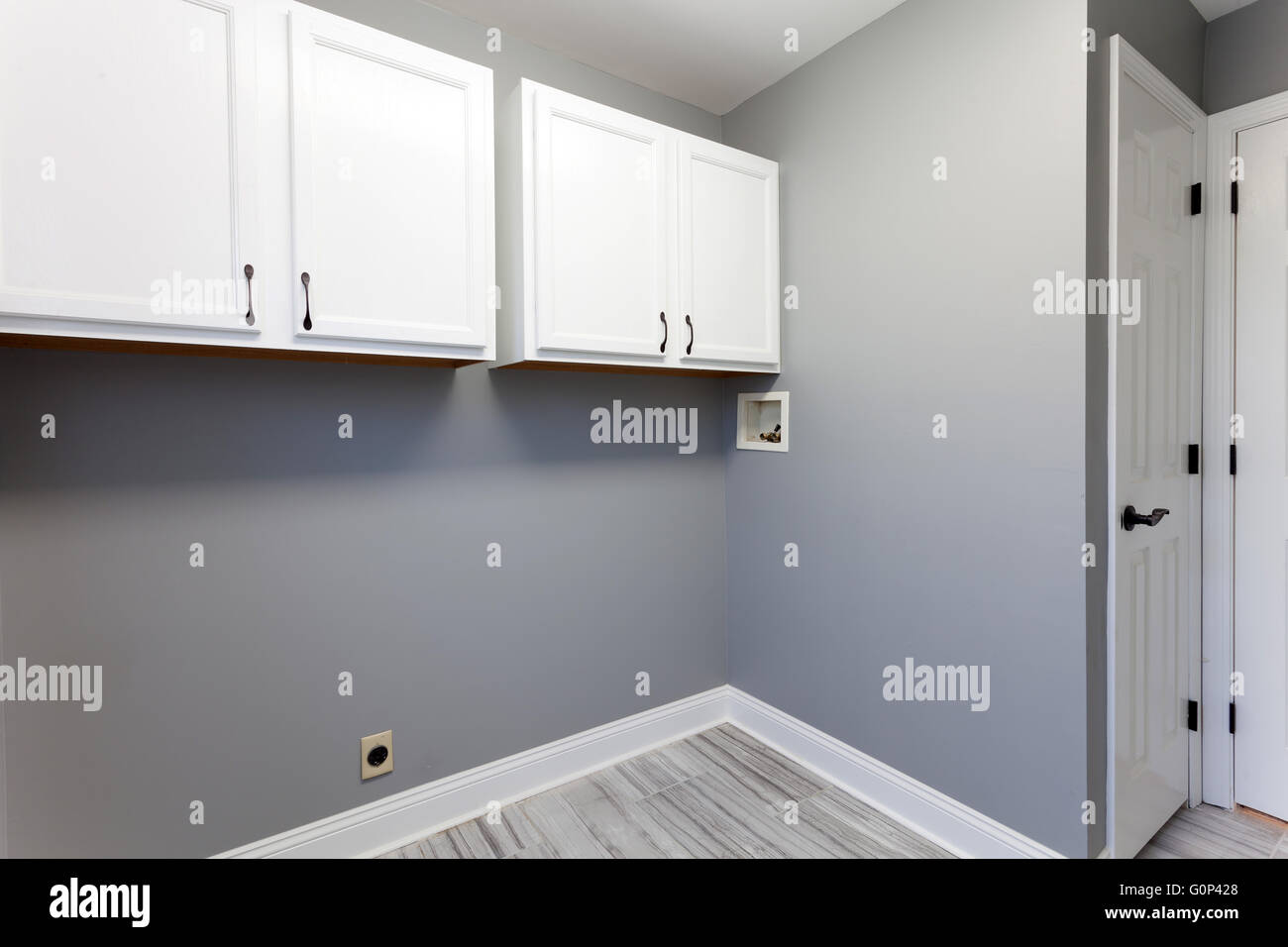 Empty laundry room setup with electrical plumbling hookups and cabinets in a modern home. Stock Photo