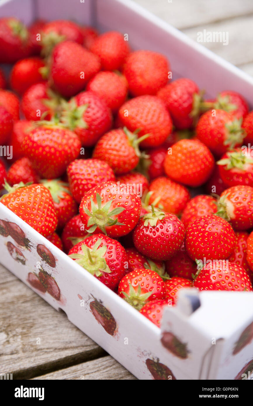 Fresh strawberries in a cardboard carton outside on a wooden table