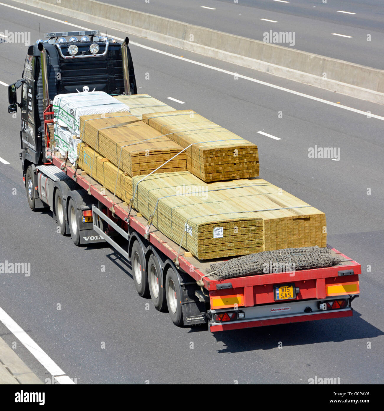 Transport logistics via flat bed articulated trailer and lorry loaded with timber building materials driving along English UK motorway Stock Photo