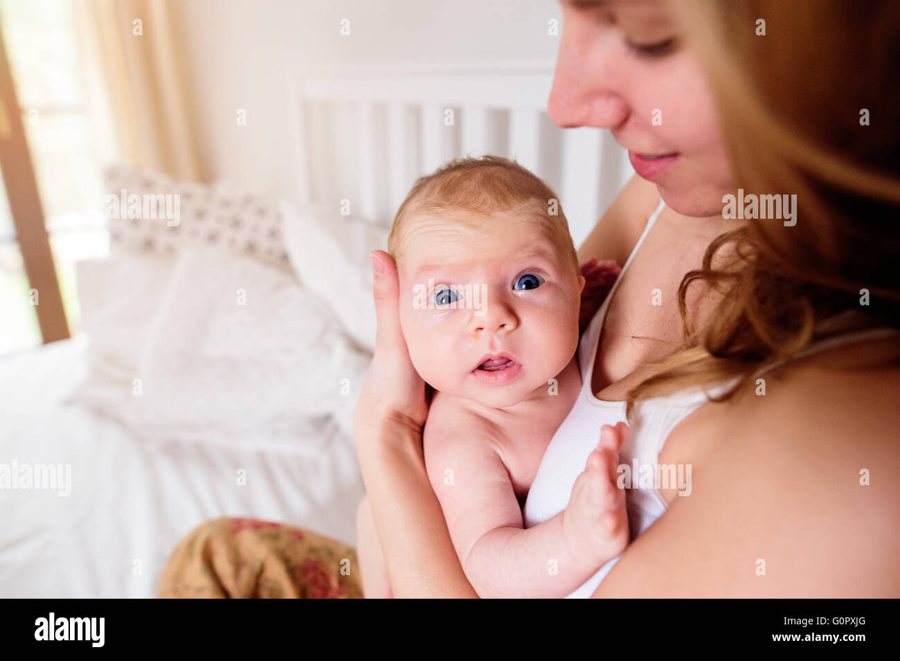 Young mother holding her newborn baby son, home bedroom Stock Photo