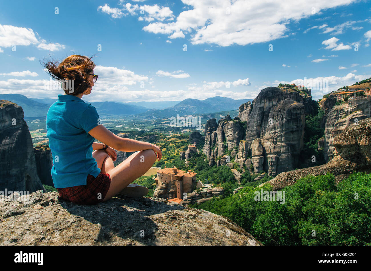 Girl sitting on the view point of the mountain. Traveler enjoying the landscape from mountain, Meteora, Greece Stock Photo