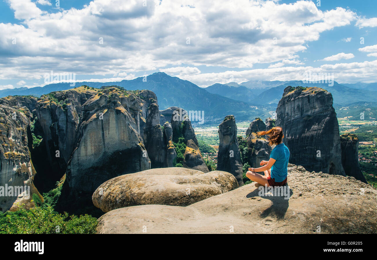 Young woman sits on top of the mount and looks at the rocks. Traveler enjoying the mountain landscape of Meteora, Greece Stock Photo