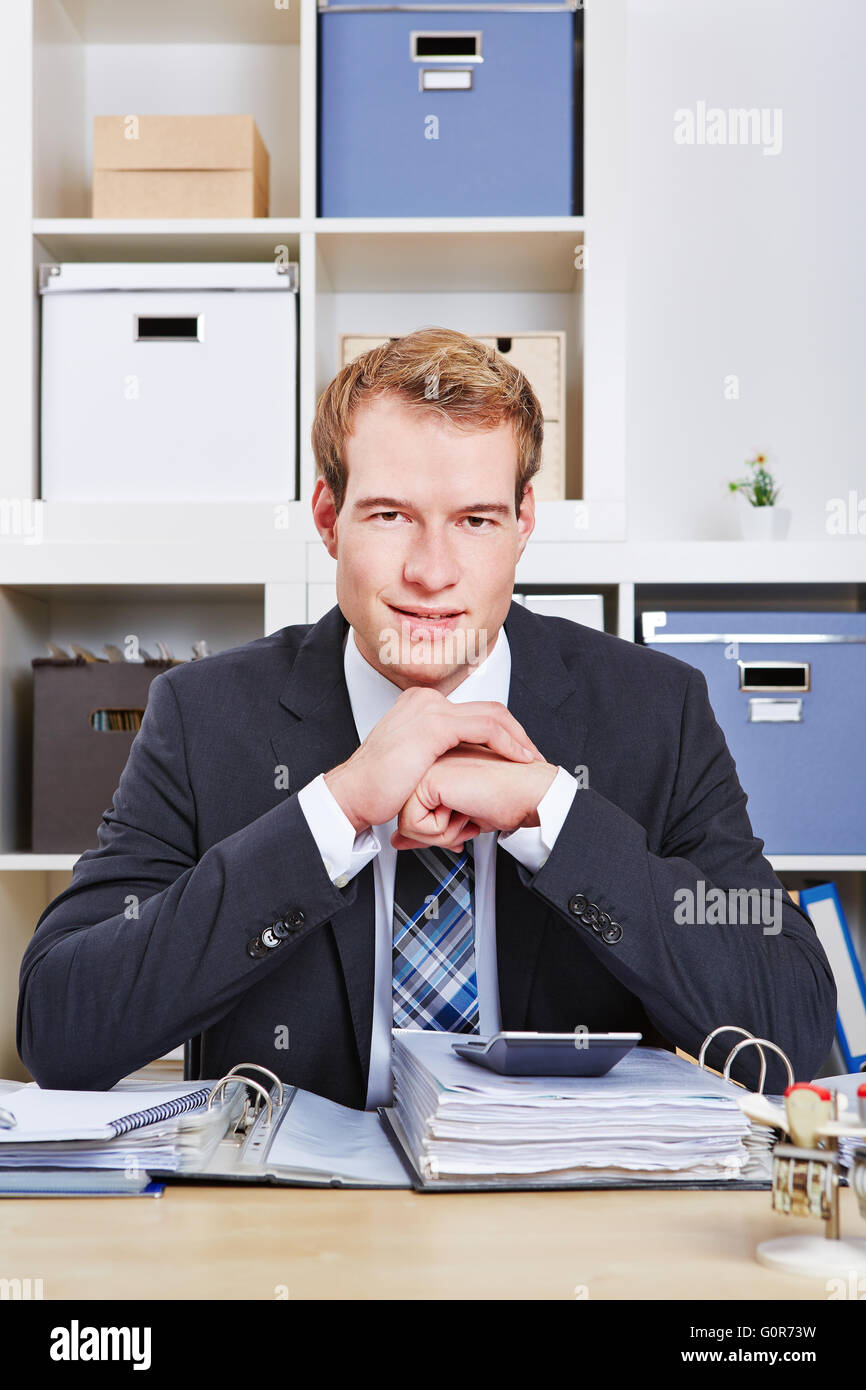 Smiling business man sitting at desk in office with files Stock Photo ...