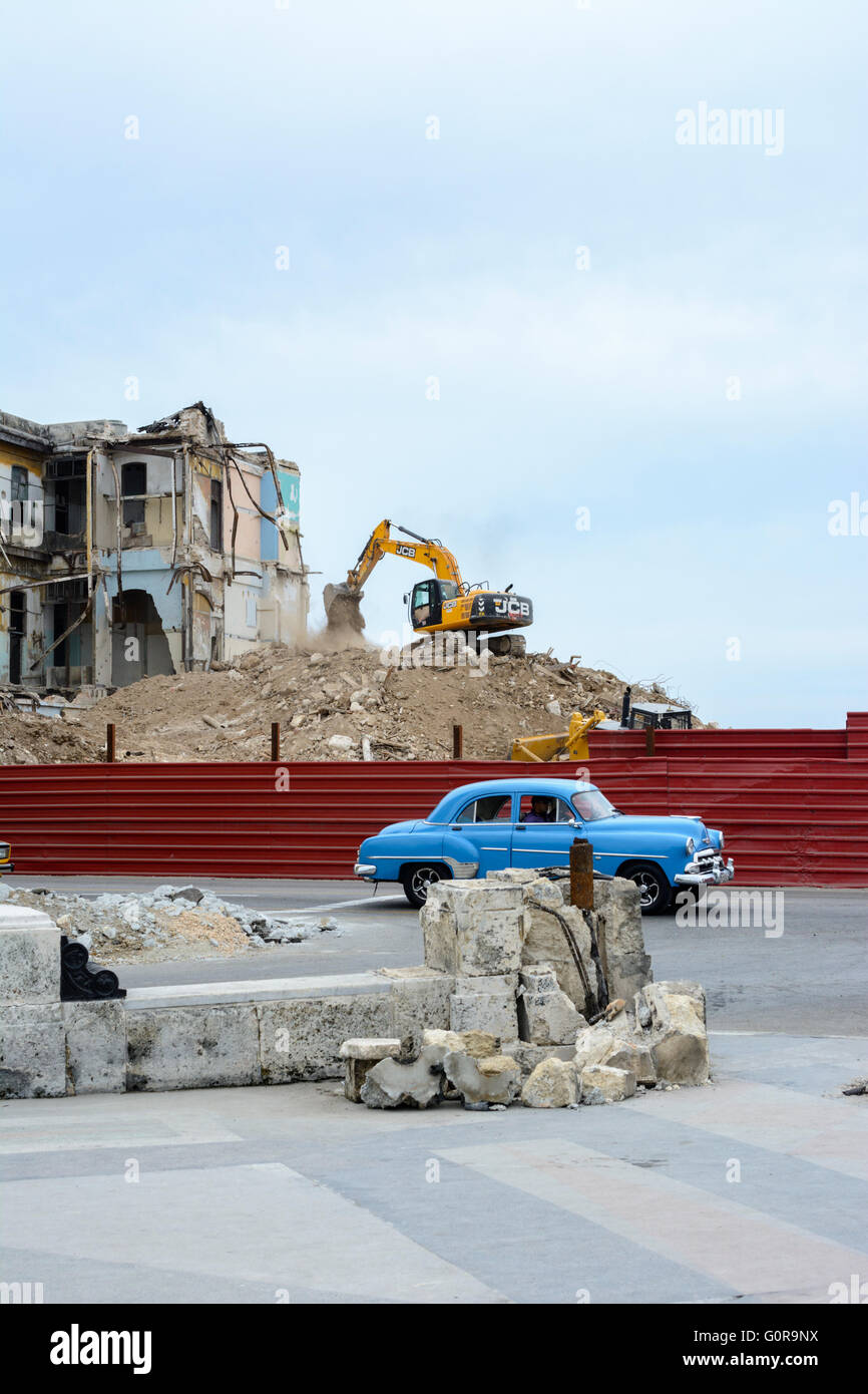 A classic American car passes a demolition site where an old building is being destroyed by a bulldozer in Havana, Cuba Stock Photo