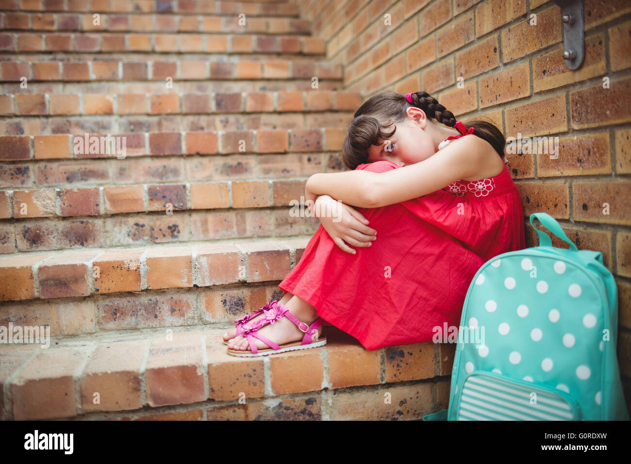 Sad brunette girl seated against a brick wall Stock Photo