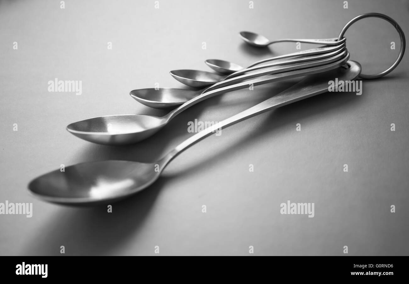A set of brushed stainless steel measuring spoons on a plain background Stock Photo