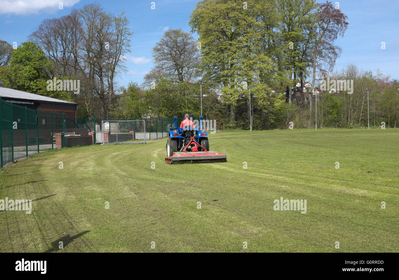 a groundsman uses a machine to cut the grass of a cricket field at