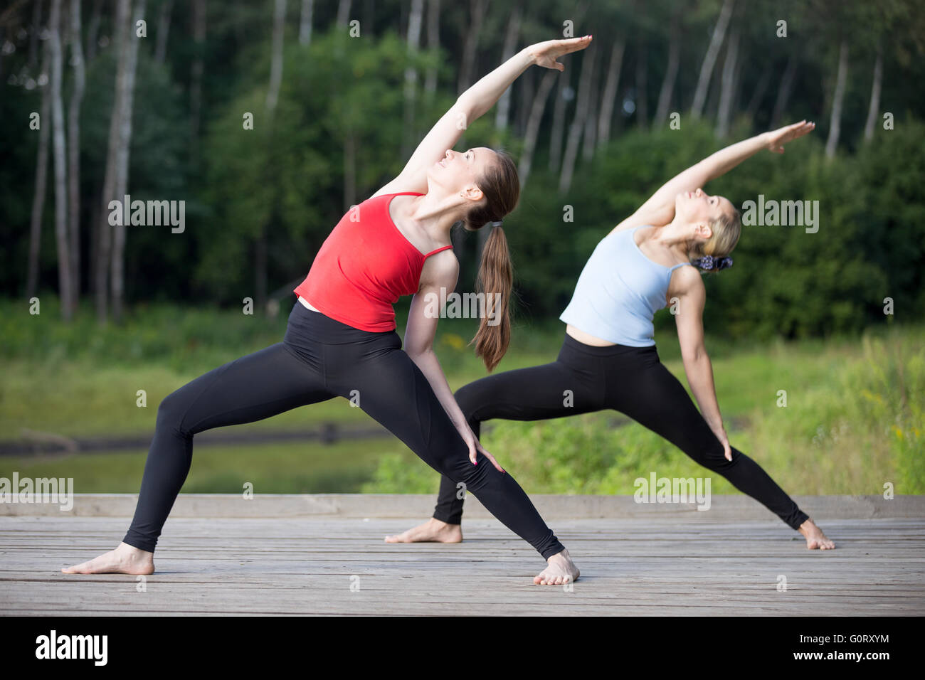 Two happy smiling sporty young beautiful women working out outdoors in park on summer day, wearing sportswear Stock Photo