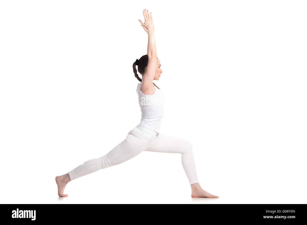 Sporty beautiful young woman in white sportswear doing lunge exercise, Warrior I posture, Virabhadrasana 1, profile view Stock Photo