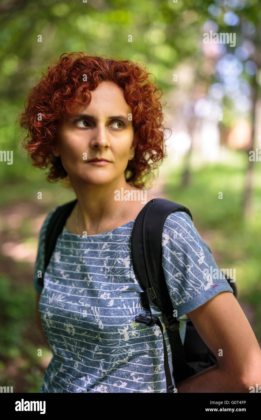 Closeup of a curly redhead woman with backpack outdoor in the forest ...