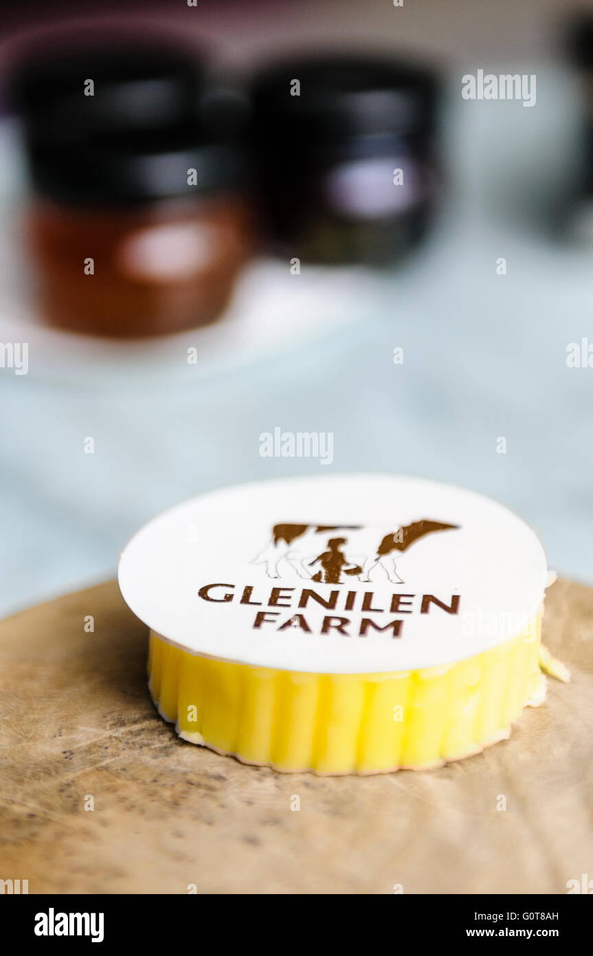 A piece of Glenilen Farm Irish cream butter on a wooden bread board with jams in a hotel restaurant. Stock Photo