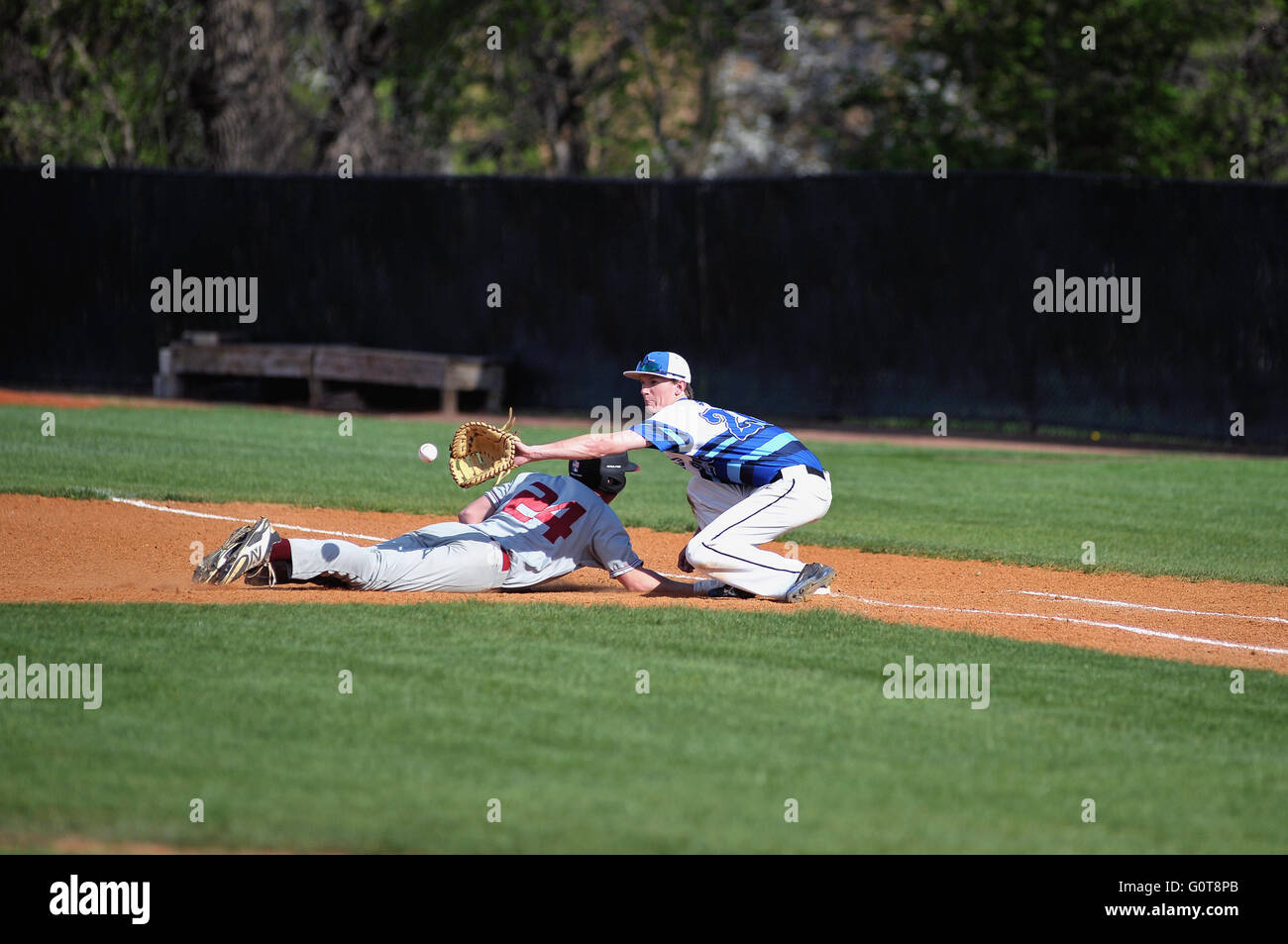 First baseman taking a pick-off throw from his pitcher as dives back safely to first base during a high school baseball game. USA. Stock Photo