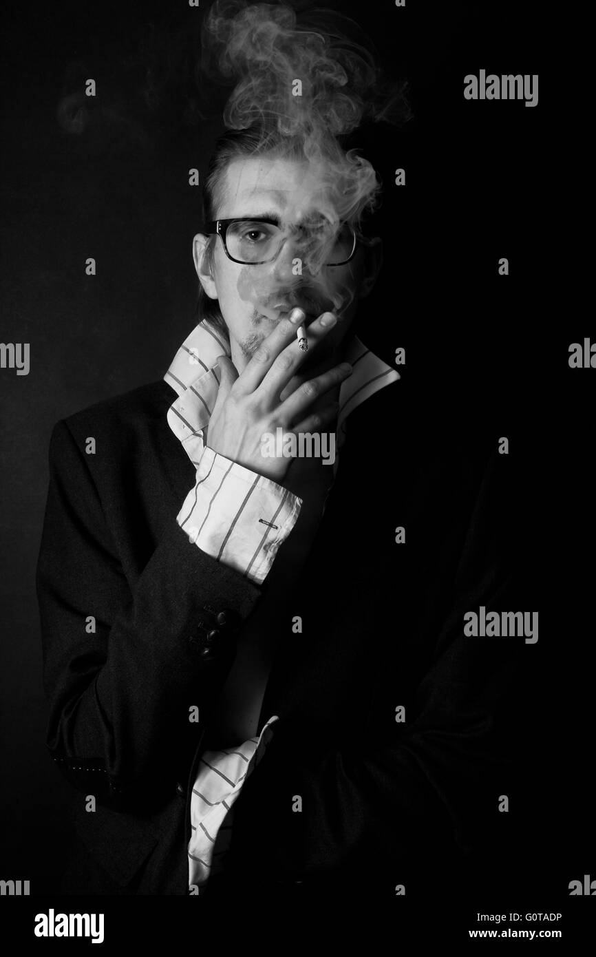 Classic portrait of young man in glasses with cigarette on black background Stock Photo