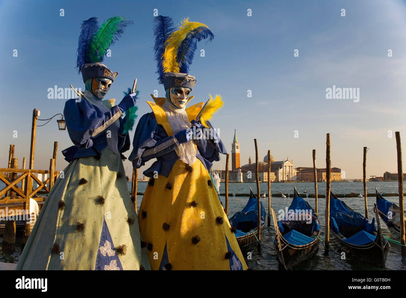 San Marco, Venice, Italy: elaborately-costumed Carnival revellers by the Basin of St Mark, with gondolas and the Chiesa di San Giorgio Maggiore beyond Stock Photo