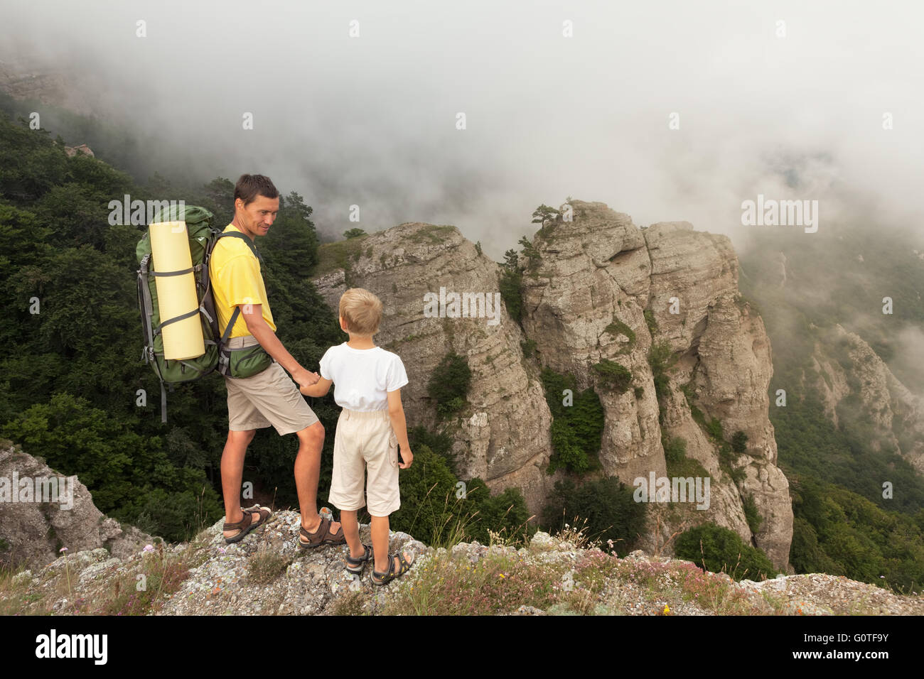 Backpacker with little son in the foggy mountains. Stock Photo