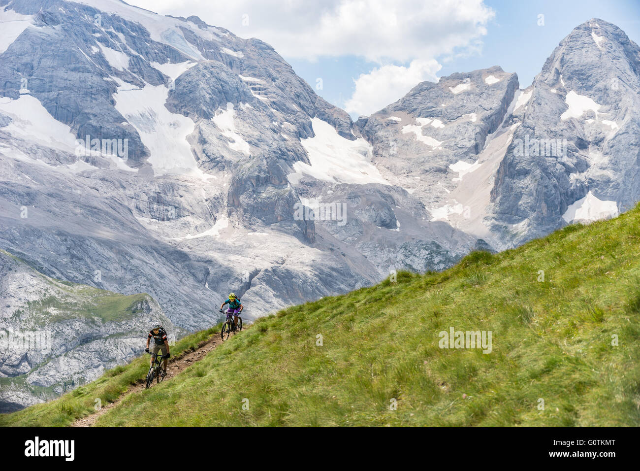 Man and woman riding mountain bikes along trail, Dolomites, Italy Stock Photo