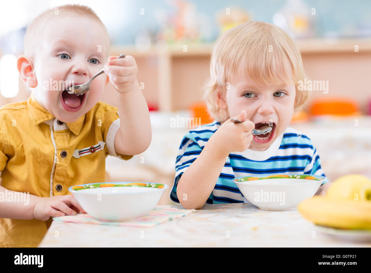 Funny little kids eating from plates in kindergarten Stock Photo