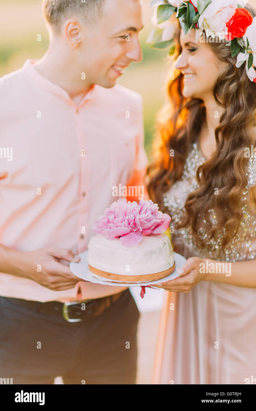 Couple celebrating at picnic, young man and woman holding cake decorated with pink flowers, close-up Stock Photo