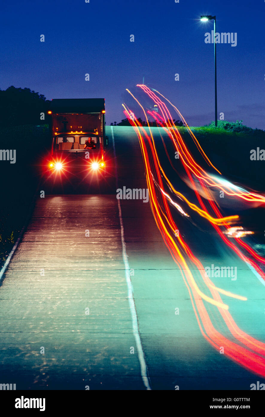 Trucks traveling on road at night  leave streaks of colorful lights Stock Photo