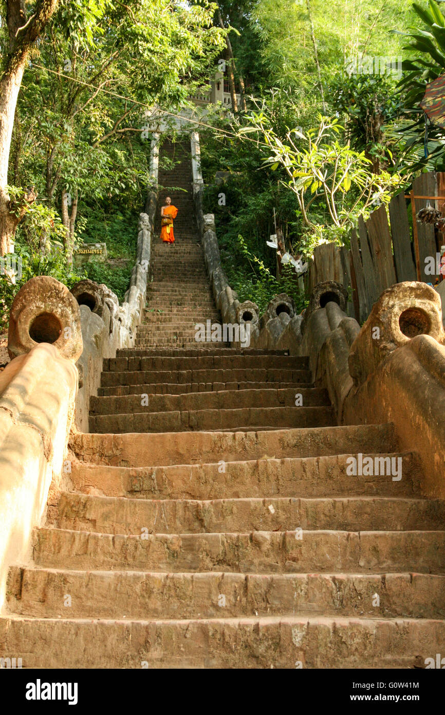 Young monk in orange robes descending the steps from Phu Si temple, Luang Prabang Stock Photo