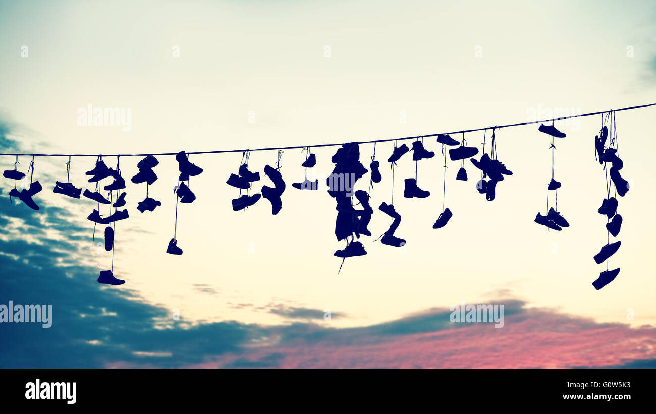 Retro stylized silhouettes of shoes hanging on cable at sunset, teenage rebellion concept. Stock Photo