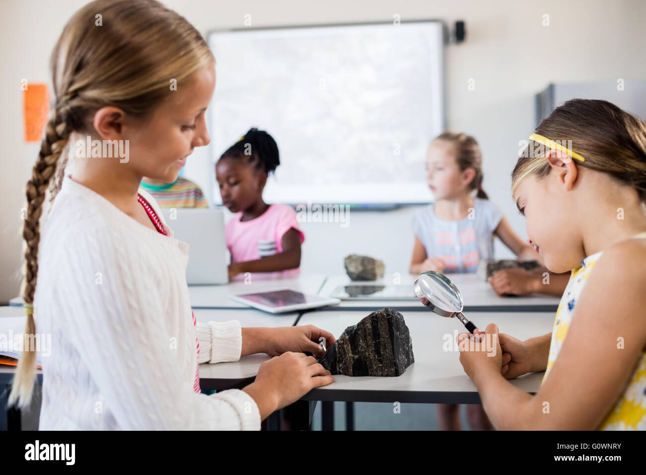 Profile view of girls looking at rock with magnifying glass Stock Photo