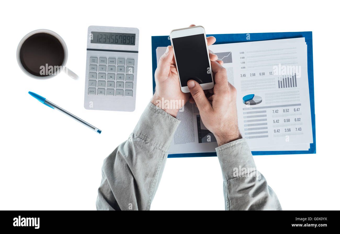 Businessman at desk using a touch screen smart phone, calculator and financial report, hands top view Stock Photo
