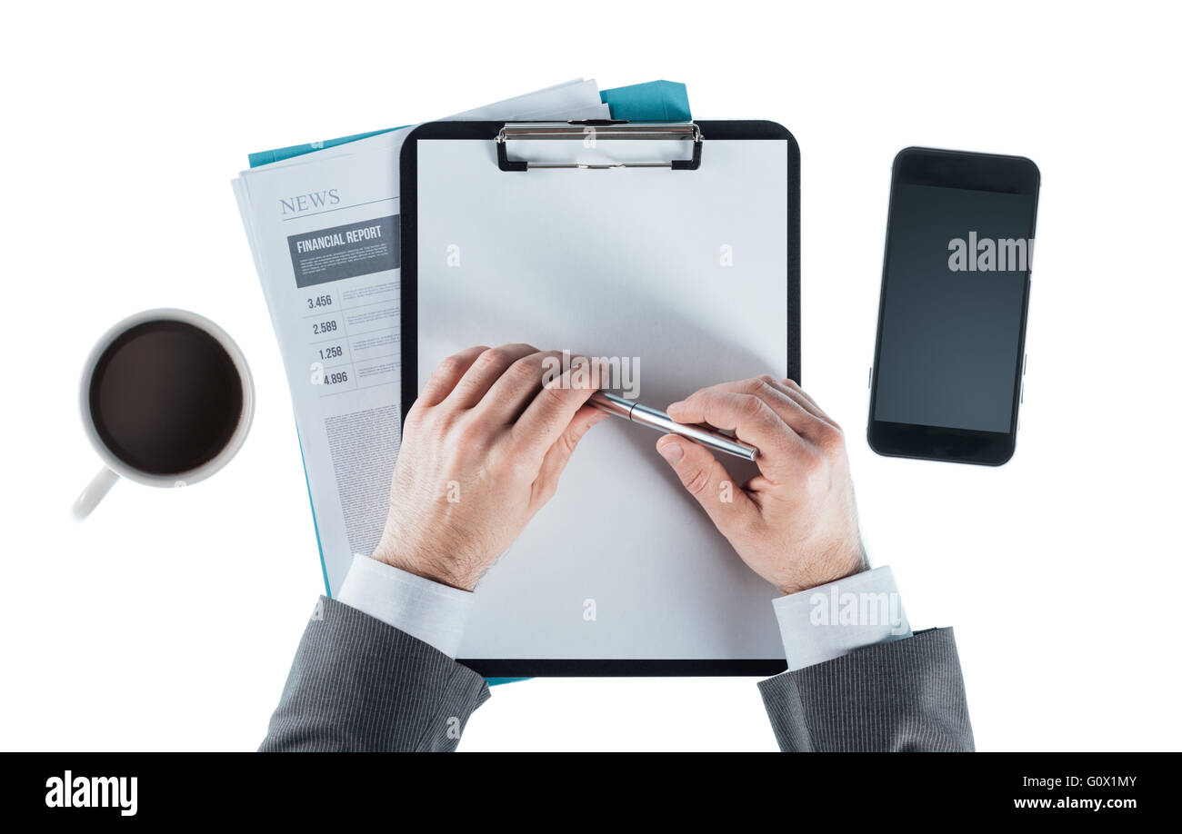 Businessman at desk holding a pen with clipboard, smartphone and coffee Stock Photo