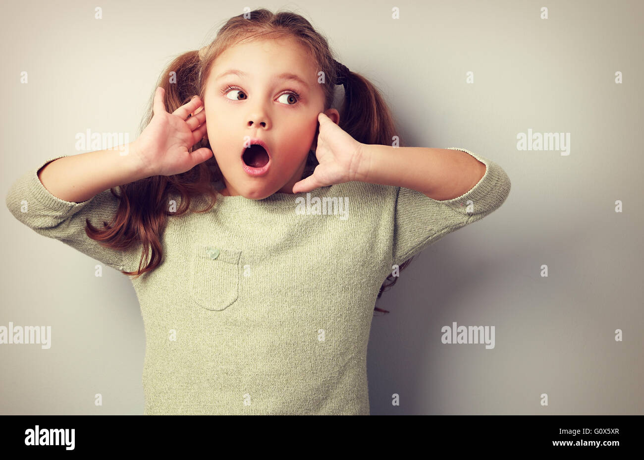 Surprising kid girl with long hair with opened mouth and hand near face looking. Toned portrait Stock Photo