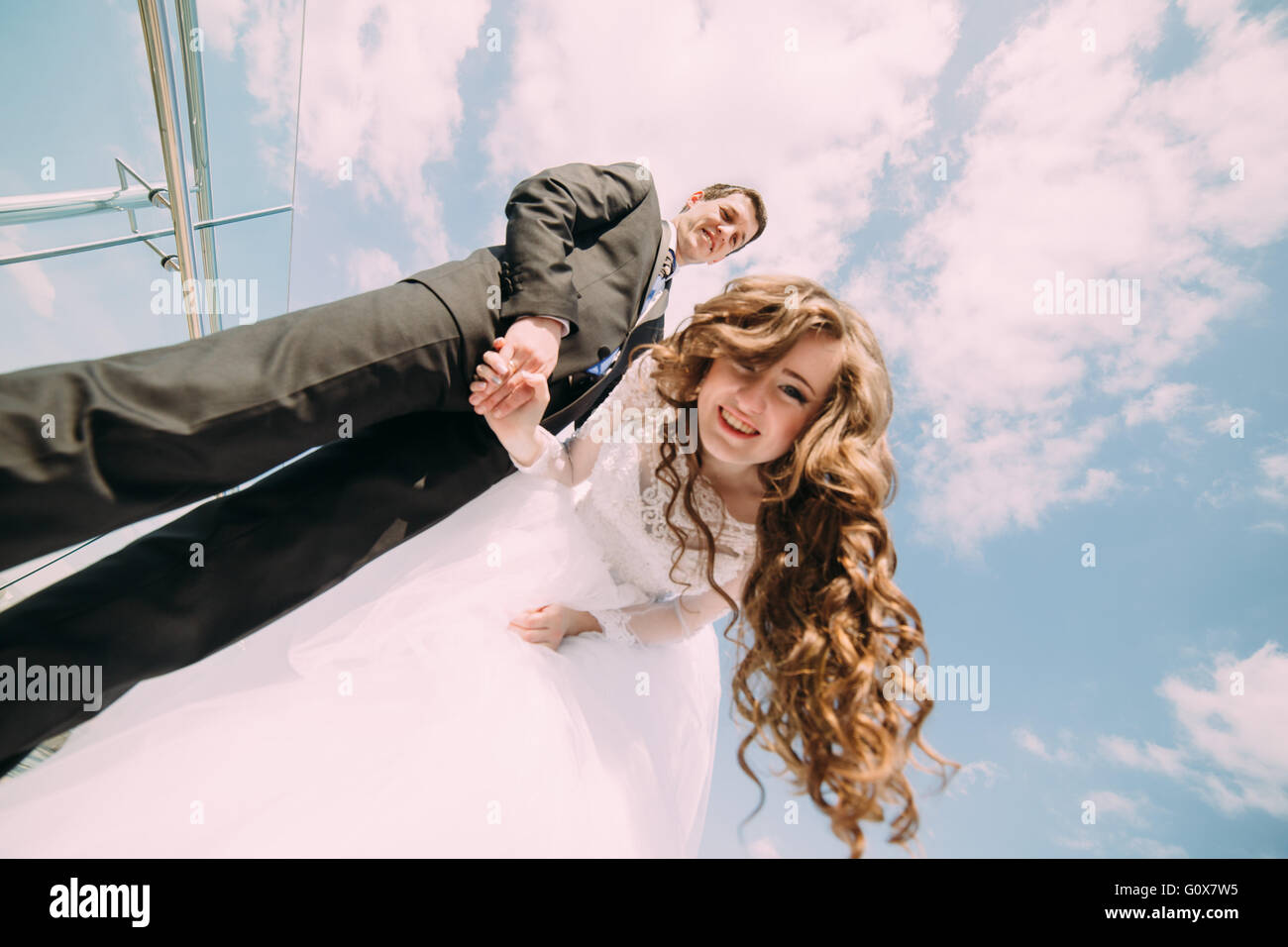 Smiling bride and groom posing for the camera against blue sky with ...