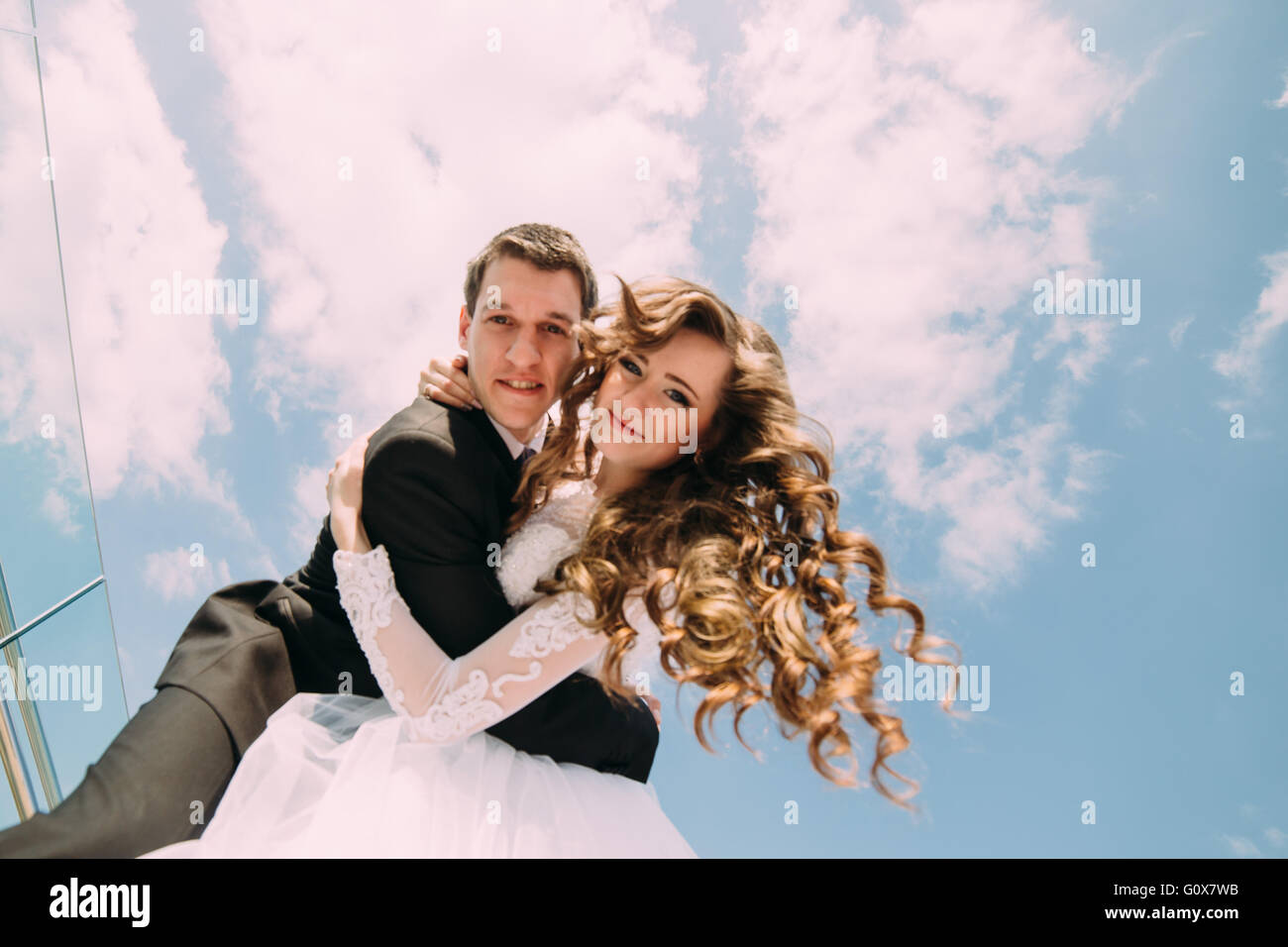 Smiling bride and groom posing for the camera against blue sky with ...
