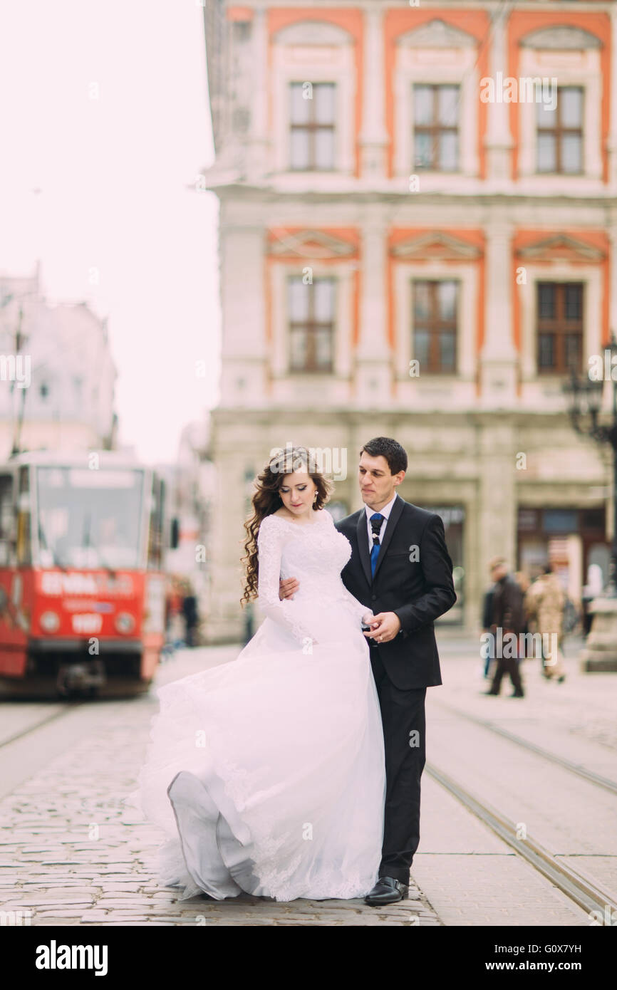 Happy groom and bride walking the streets of the old city with tram on ...