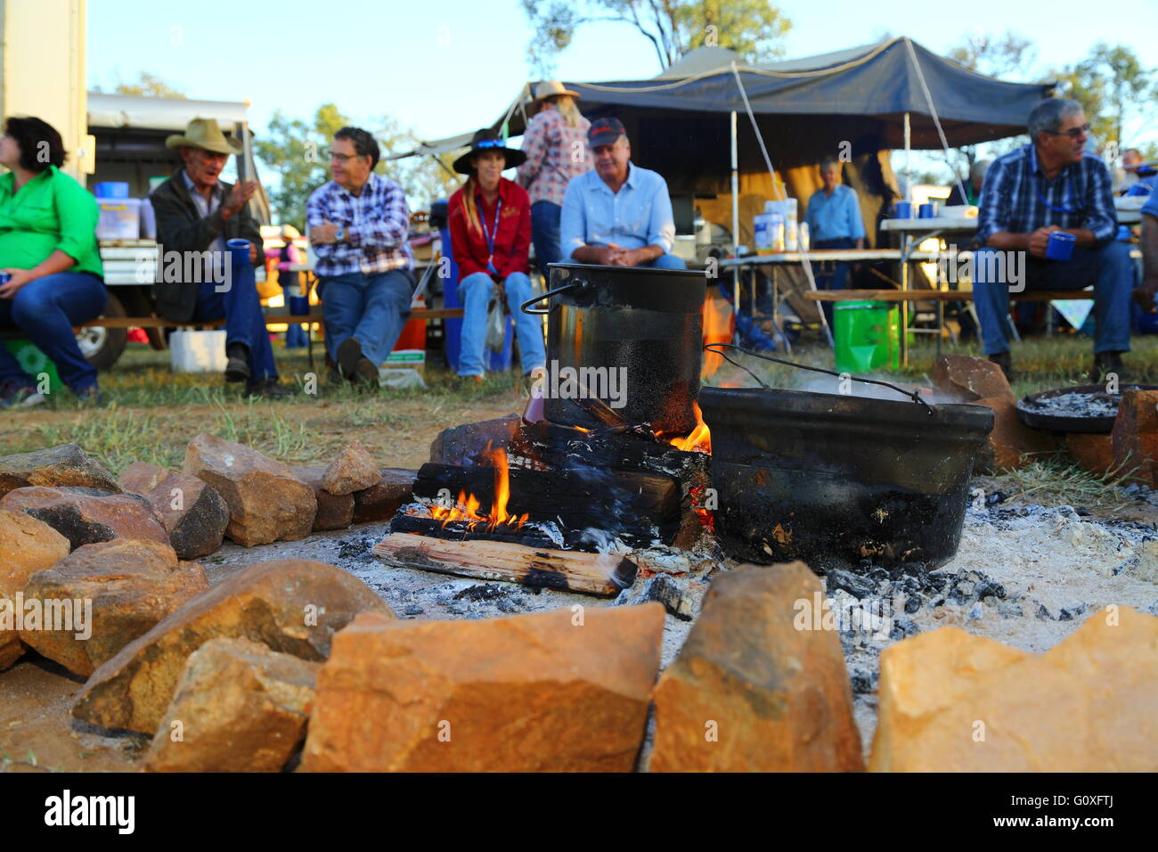 A group of horse riders chatting around a morning camp fire as water boils in big pots during a cattle drive near Eidsvold, QLD. Stock Photo