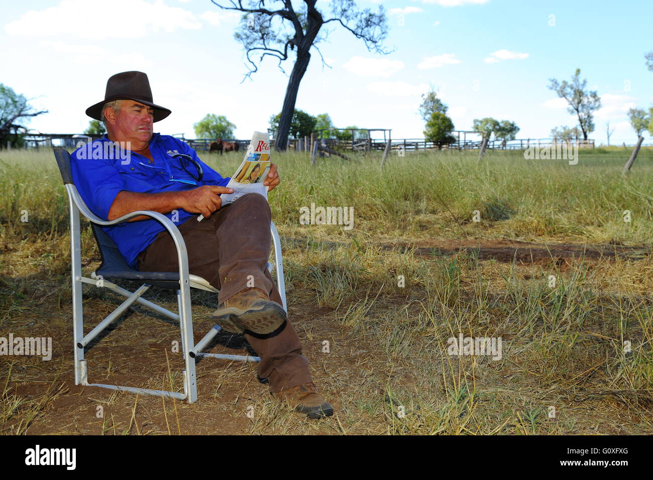 A middle aged farmer reading the newspaper in the shade of a tree on a farm near Eidsvold, Queensland. Stock Photo