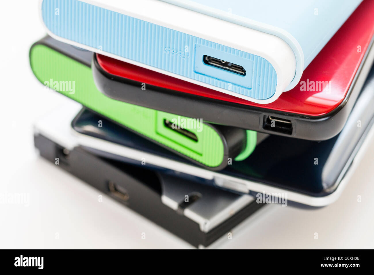 Five different and various coloured external portable hard drivers stacked up showing end with USB connection points. No brand name. White background. Stock Photo