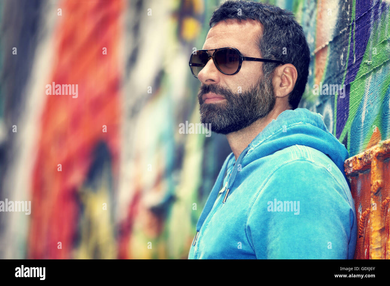 Portrait of a handsome man with stylish beard and sunglasses, standing over colorful city wall background, fashion street look Stock Photo