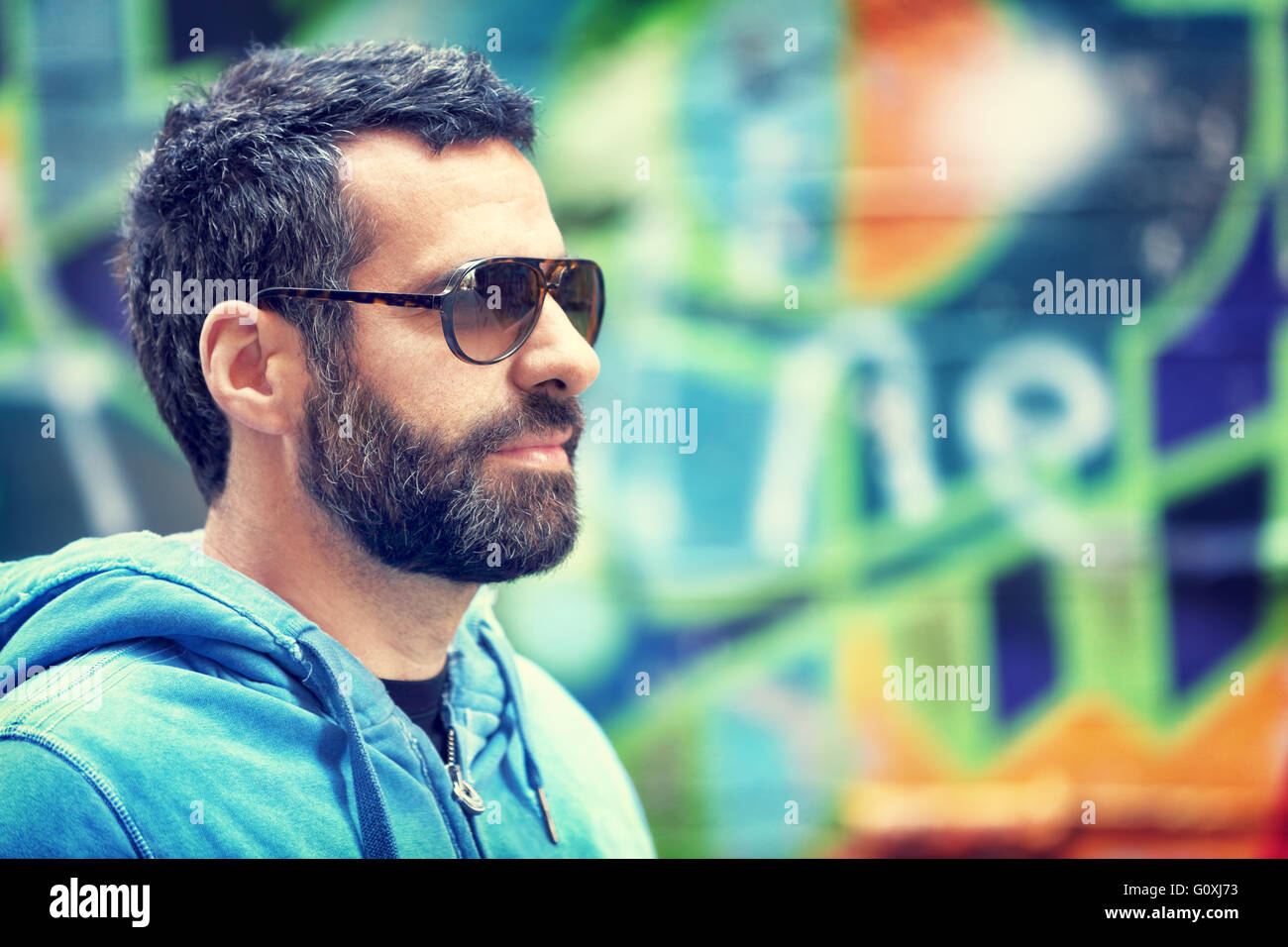 Closeup portrait of handsome man with stylish beard and sunglasses, standing over colorful city wall background Stock Photo