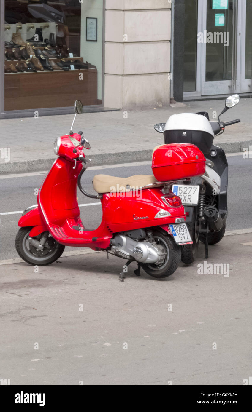 Two motor scooters, one red, one black and white, parked on a street in