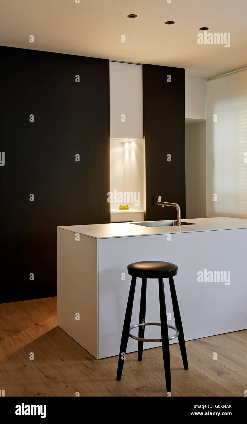 Modern white countertop with sink and stainless steel mixer tap. Black stool next to counter. Stock Photo