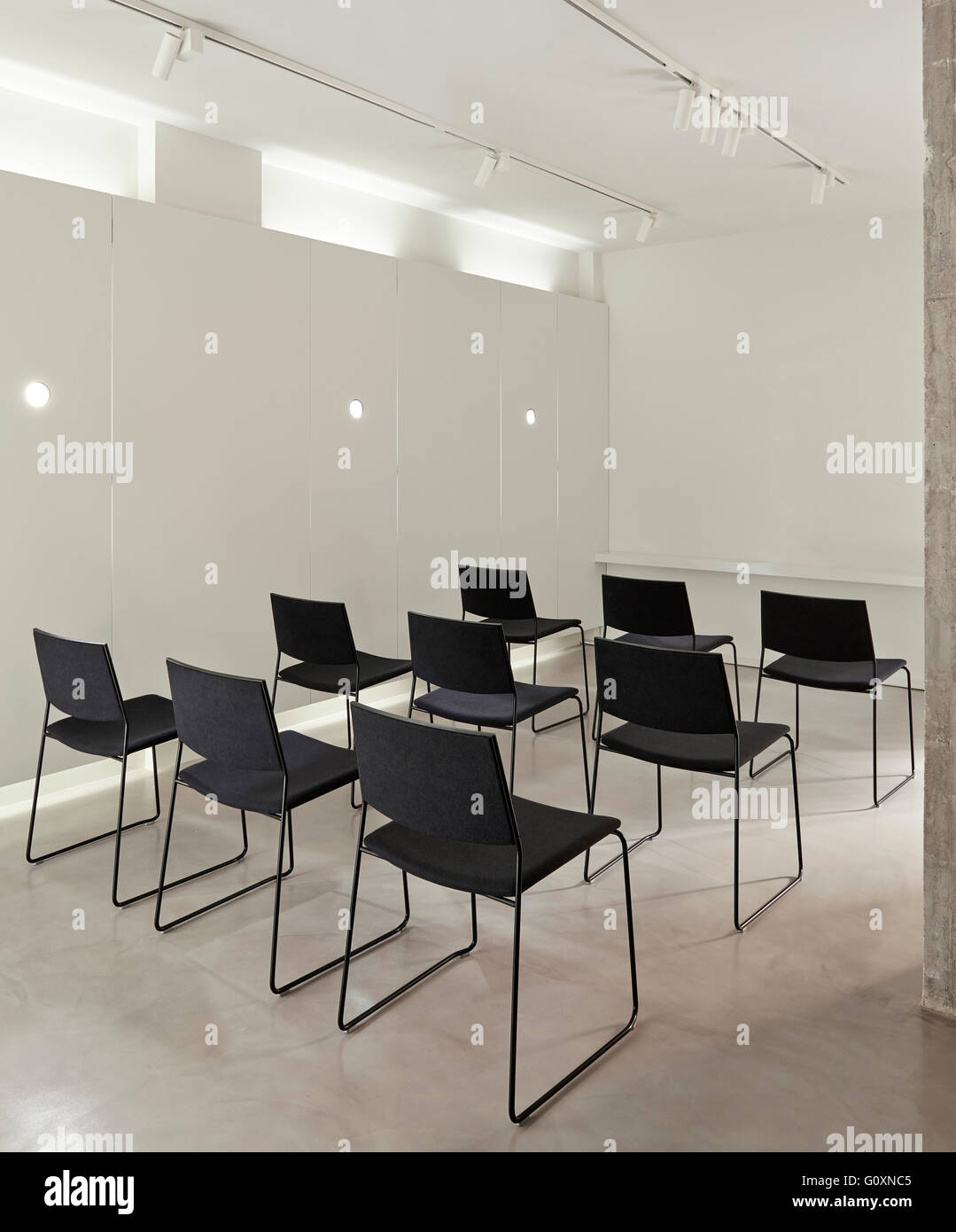 RI Gallery, Barcelona, Spain. Chairs lined up in rows in white modern room. Screen in front of