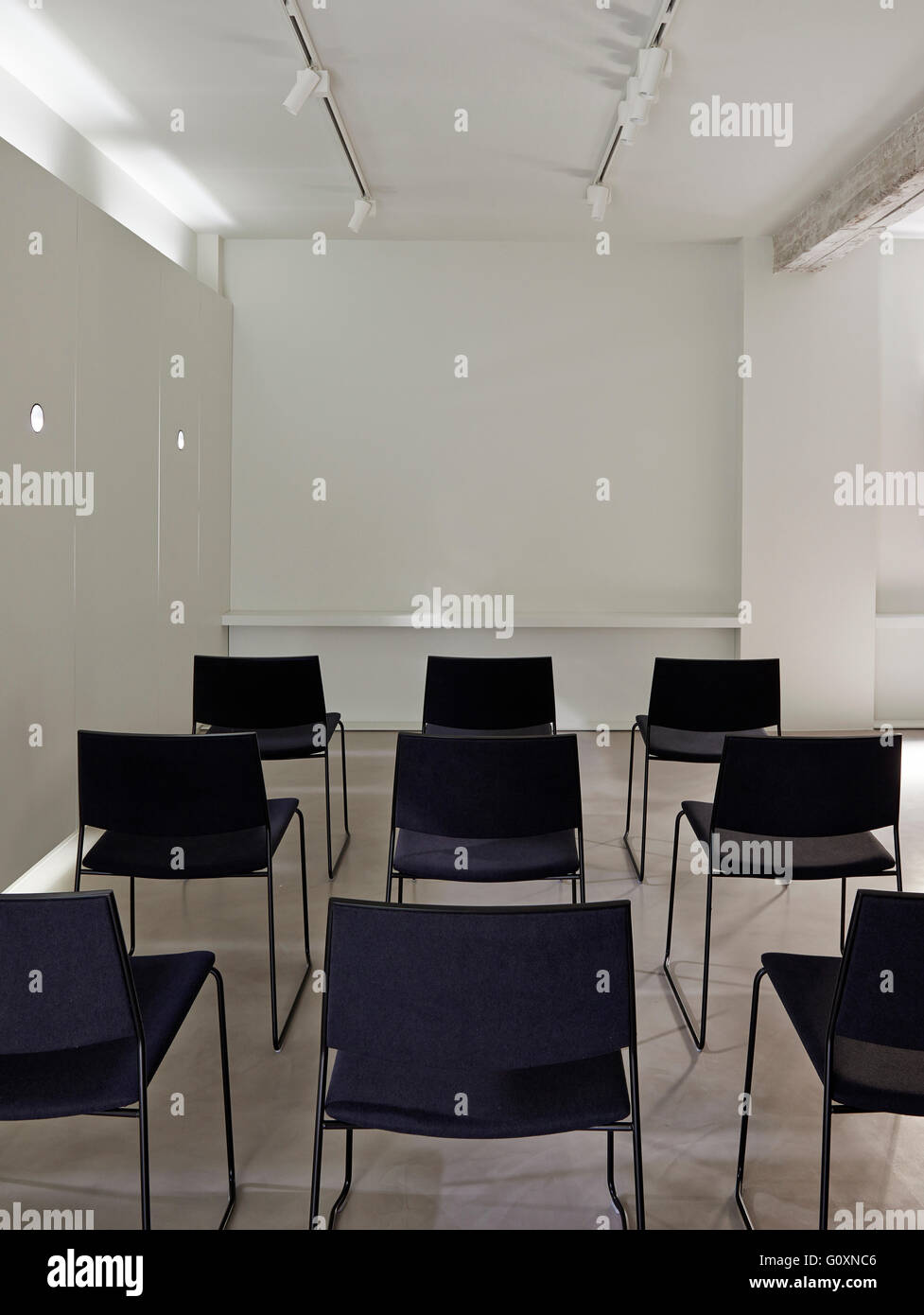 RI Gallery, Barcelona, Spain. Chairs lined up in rows in white modern room. Screen in front of