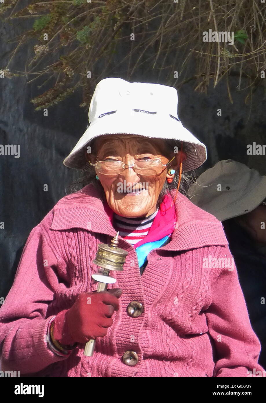 Tibetan old lady with a hand prayer wheel and chanting mantras while on her way to the monastery to offer her prayers. Stock Photo