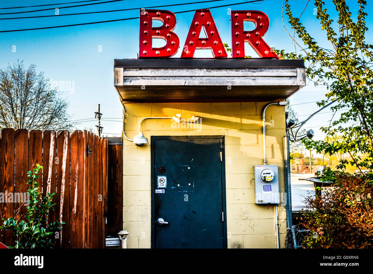 A low concept industrial edge to A back door entrance to a Dive bar with a huge red sign 'BAR' on roof seems odd and arty Stock Photo