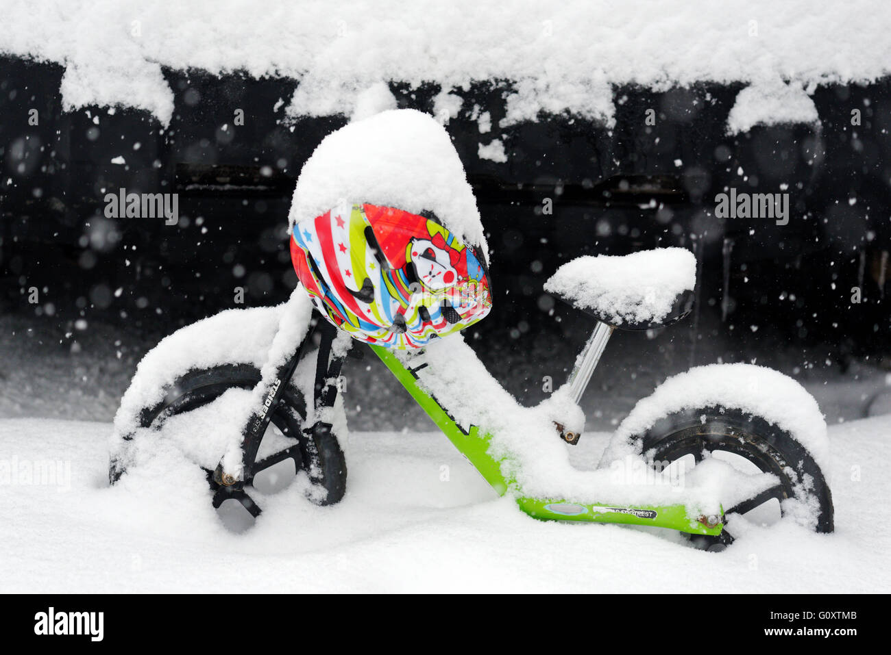 A child's balance bike and helmet covered in snow Stock Photo
