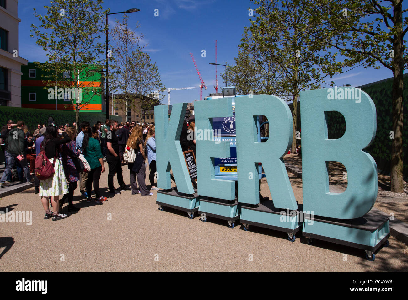 A long line of people queuing next to a large sign for food at a popular London street food market known as The Kerb. Stock Photo