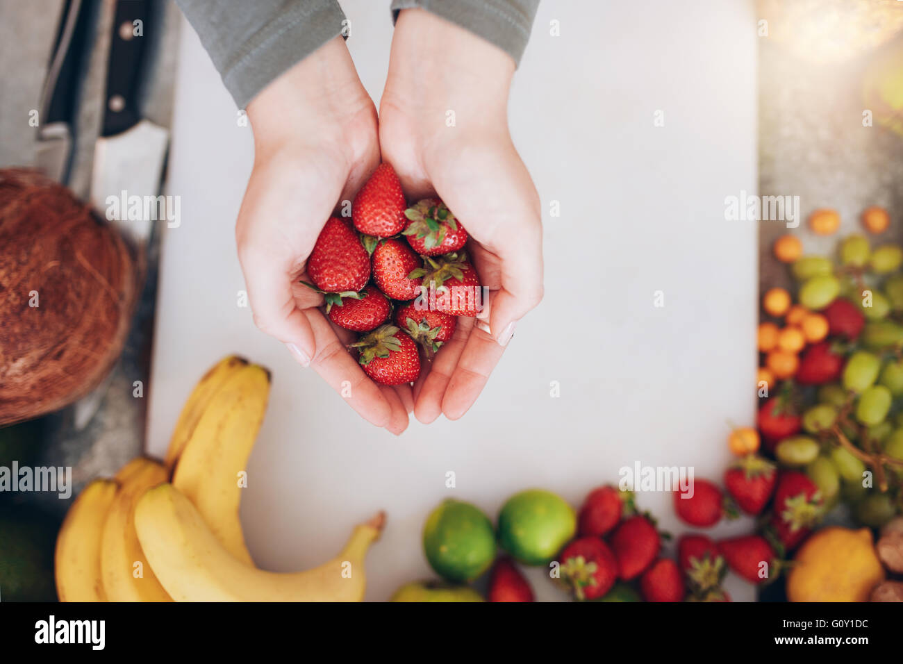 Top view close up shot of a woman's hands holding fresh strawberries over shopping board with fruits. Female holding a handful o Stock Photo