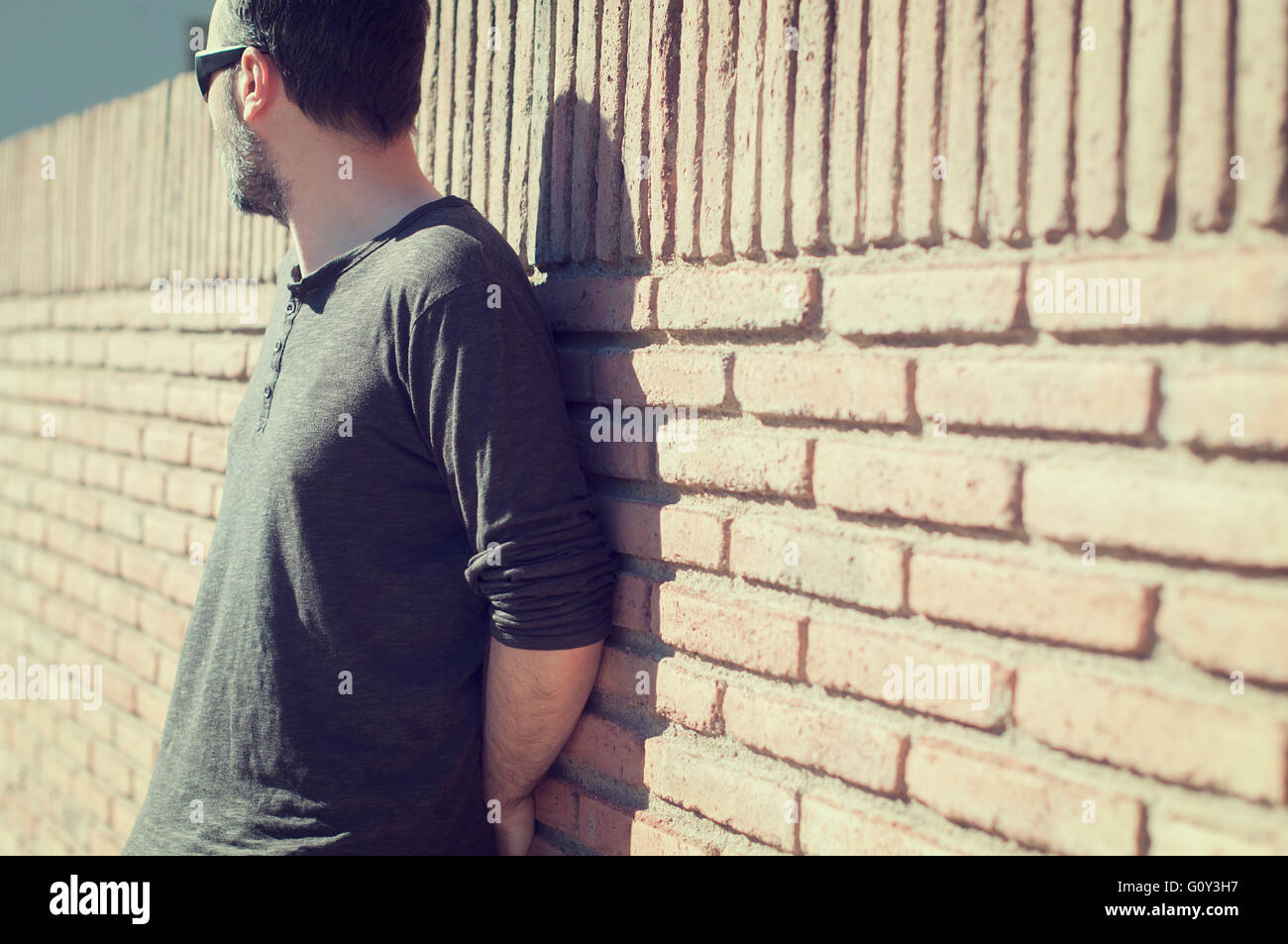 Man wearing sunglasses leaning against a wall outdoors Stock Photo - Alamy